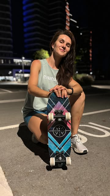 Mari kneeling beside a skateboard before an outdoor workout.
